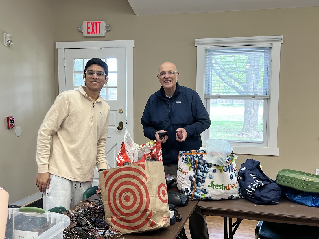 Two volunteers with shopping bags and a bin of eyeglasses collected from local optical stores