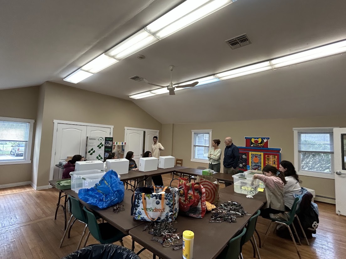 Girl Scout volunteers sorting bagged eyeglasses into bins across a hall of tables
